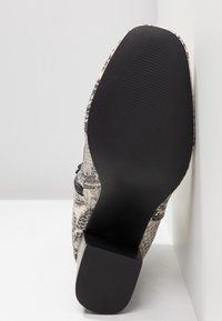 Vue de la semelle d'une bottine à talon haut avec une semelle noire texturée et un matériau supérieur à motif peau de serpent.