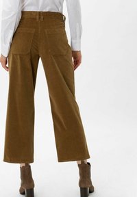 Brązowe szerokie spodnie kordrowe z tylnymi kieszeniami, charakteryzujące się gładką teksturą i widocznym prążkowanym wzorem, zestawione z brązowymi botkami na obcasie.