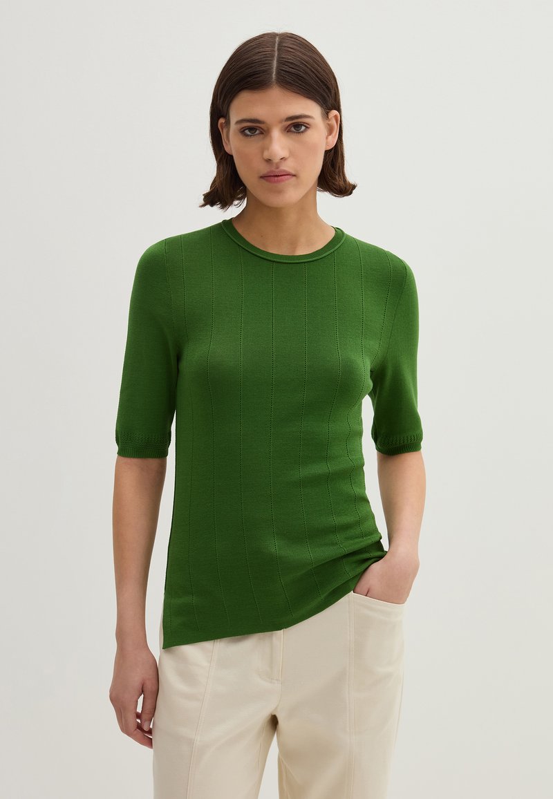 Maglione corto a maniche corte in maglia rigata verde con scollo rotondo, caratterizzato da una sottile trama e una silhouette aderente. Abbinato a pantaloni di colore chiaro.