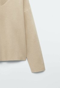 Maglione beige a maniche corte con scollo a V ampio. Texture morbida e liscia; vestibilità rilassata con lunghezza cropped e design a spalle rientrate.