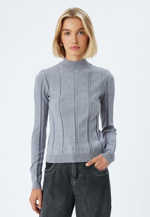 Grå striktrøje med ståkrave, prydet med lodret ribbet struktur og lange ærmer, kombineret med mørkegrå denimbukser.
