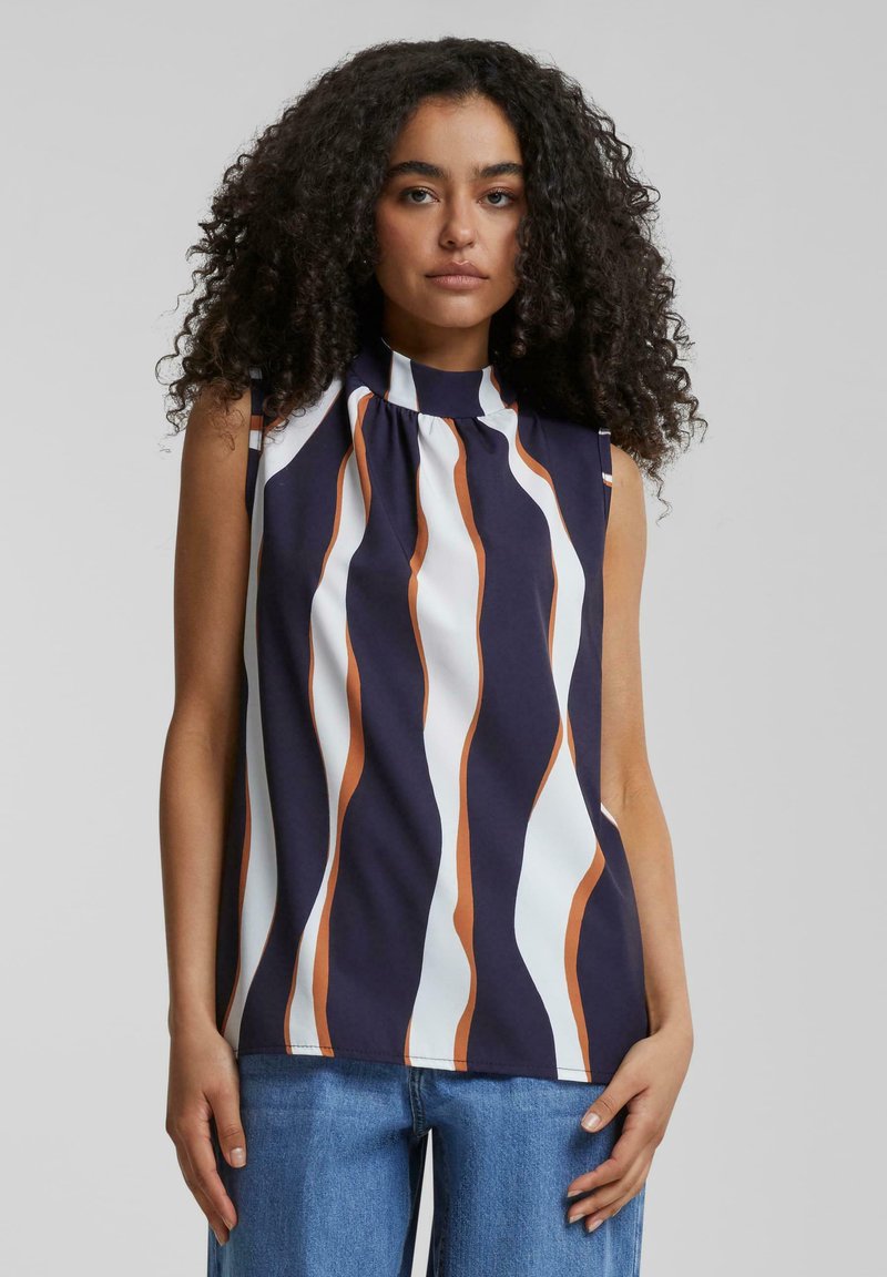 Blouse sans manches avec un col montant, présentant des rayures verticales ondulées en marine, blanc et rouille. Tissu lisse avec des détails de plis au niveau du col.