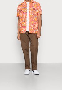 Kortærmet orange skjorte med farverige mønstre, parret med brune bukser, båret med hvide sneakers og en enkel hvid t-shirt under.