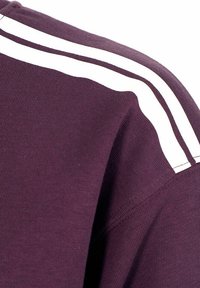 Felpa color bordeaux con strisce doppie bianche lungo le spalle. Il tessuto appare a coste e ha una consistenza morbida con una vestibilità classica.