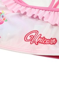 Haut de maillot de bain rose avec bordure froncée, présentant un design de licorne et des accents floraux. Texte "Licorne" en rouge en bas à gauche. Matière douce.