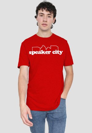 Red short-sleeve t-shirt made of cotton blend; features white printed text "speaker city" with a skyline graphic above it.