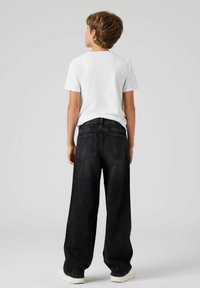 Pantalons en denim noir à coupe loose, dotés de deux poches arrière, associés à un T-shirt blanc simple et des baskets blanches.