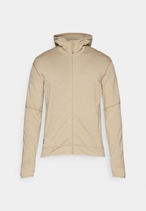 Beige zip-up jacka med hög krage, långa ärmar och flatlock-sömmar. Mjuk textur, minimalistisk design med en liten logotypdetalj.