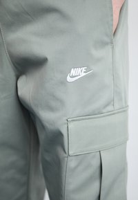 Ανοιχτοπράσινα cargo παντελόνια από λείο ύφασμα, με θήκη, πλευρικές πτυχές και λευκό λογότυπο Nike στο μηρό.