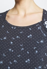 Dark gray top featuring a scoop neckline, decorated with light blue floral and polka dot patterns, and a button detail on the shoulder.