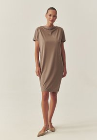 Šaty s krátkými rukávy a délkou ke kolenům v světle hnědé barvě, vyrobené z hladké elastické látky a s jednoduchým, volným střihem.