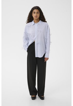 Camicia a righe blu chiaro e bianca con vestibilità oversize, decorata con fiocchi ricamati sulle maniche, abbinata a pantaloni neri a vita alta.