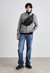 Γκρίζα φούτερ με φερμουάρ και υφασμάτινο σχέδιο, μαύρος ψηλός γιακάς, μπλε τζιν και μαύρη τσάντα χιαστί. Το σύνολο ολοκληρώνεται με μαύρα αθλητικά παπούτσια.