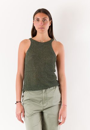 Giovane donna vista frontalmente che indossa un top verde a maglia senza maniche e pantaloni verde chiaro su sfondo bianco.