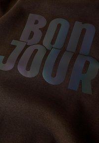 Il tessuto nero presenta un grande testo che riporta la scritta "BON JOUR" in sfumature di colore, con una texture liscia e un design audace e moderno.