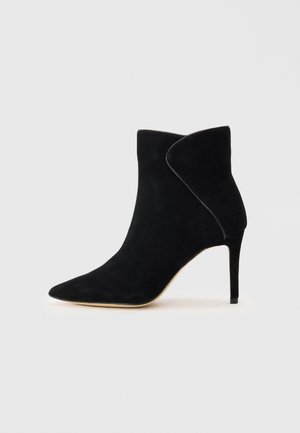 Botte chelsea en suède noire avec un bout pointu, un design d'ouverture latérale et un talon haut élancé. Texture lisse et silhouette minimaliste.