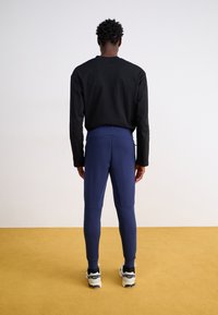 Sort langærmet skjorte parret med tætsiddende navy leggings, lavet af strækbart stof, der har en glat tekstur og er fremhævet med et højt liv.
