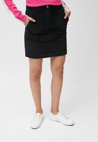 Sort corduroy nederdel med lommer, der har knaplukning og en lige skåret design. Båret med hvide sneakers.