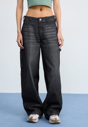 Svarta denim cargo shorts med en lös passform, synlig sömnad och sidofickor. Bärs med en kort grön topp och vita sneakers.