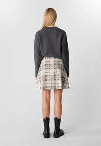 Maglione grigio con un design cropped; gonna a quadri in beige, grigio e arancione chiaro; abbinata a stivaletti neri alla caviglia con cerniere.