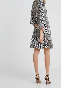 Svart-och-vitt mönstrad klänning med djurmotiv, utsvängd nederdel och trekvartsärmar. Bärs med svarta stiletto-klackar med remmar.