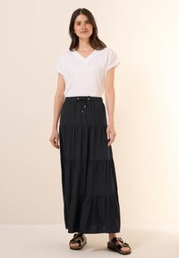 Svart, lager-på-lager maxi kjol med elastisk midjeband och justerbar dragsnöre. Kombinerad med en vit t-shirt med V-ringning och bruna sandaler.