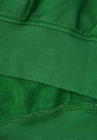 Tejido verde que consiste en una capa suave y densa de punto y una capa blanda y texturizada. Costuras visibles a lo largo de los bordes.