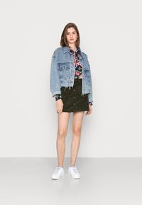 Jaqueta de ganga com bainha desfiada, blusa floral, saia de veludo cotelê verde e sapatilhas brancas. Características principais: estilo casual, texturas sobrepostas e contraste de cores.