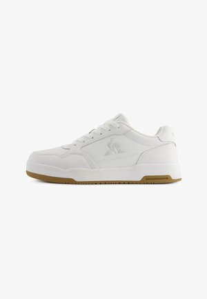 White athletic shoe made of smooth synthetic material. Features a flat sole with a textured gum rubber outsole and simple lace-up design.