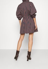 Rutigt klänning i marinblått och rött tyg med huva, insvängd midja och puffärmar, matchad med bruna klackiga ankelstövlar.