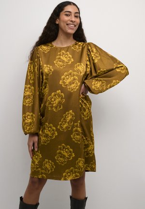 Goldfarbenes Kleid mit floralem Muster, langen puffärmel und rundem Halsausschnitt. Glattes, glänzendes Material mit knielanger Länge. Schwarze kniehohe Stiefel.