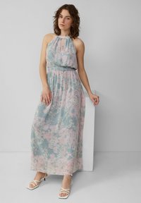 Maxi-Kleid in Hellblau mit rosa Blumenmustern, Halterneck-Design, gerafftem Bund und fließendem Rock. Getragen mit weißen Riemchen-High Heels.