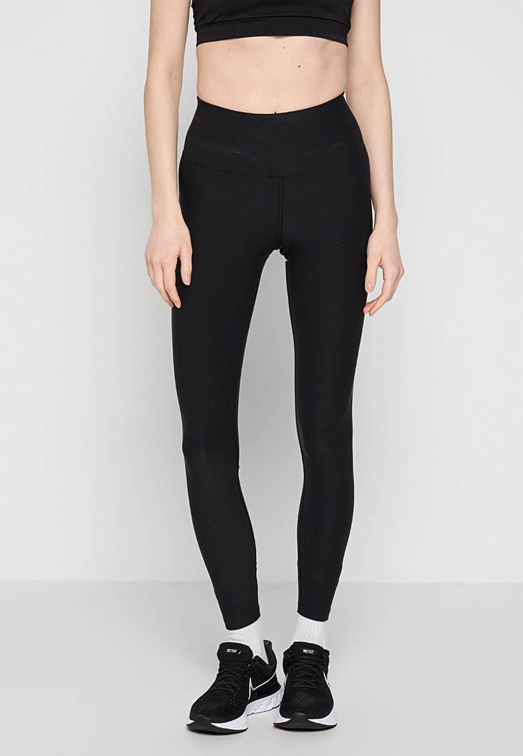 Leggings neri con vita alta, realizzati in materiale elasticizzato. Indossati con un crop top nero e scarpe da ginnastica nere con dettagli bianchi.
