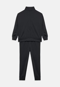 Μαύρο σετ φόρμας δύο τεμαχίων με μακριά μανίκια, μπουφάν με ψηλό γιακά και παντελόνια με στενή άκρη σε απλό λευκό φόντο.