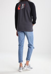 Svart och grå sweatshirt med röd Nike-logga på baksidan, tillsammans med ljusblå jeans och silverfärgade löparskor. Avslappnad och ledig passform.