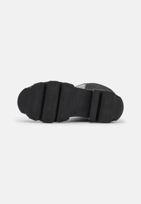 Suela de zapato negra con una superficie texturizada, que presenta estrías elevadas y una sección central lisa, diseñada para ofrecer tracción y durabilidad.