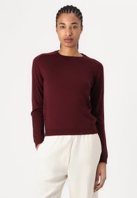 Bordeaux sweater med lange ærmer, rund halsudskæring og ribbet kant. Materialet ser blødt og let ud og bæres sammen med cremede bukser.