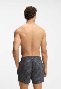 Tummansininen uimashortsikangas, jossa on geometrinen kuvio, joustava vyötärönauha, sivutaskut ja pieni logotunniste takana.