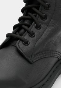 Black leather ankle boot with sturdy laces, reinforced eyelets, and textured surface. Features stitching along the sole for durability.