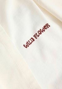 Tissu blanc avec texte marron indiquant "FLEUR SAUVAGE" en police arrondie et ludique.