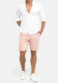 Hvid linnedskjorte med oprevet ærmer, parret med lyserøde shorts med optræk og hvide sneakers. Afslappet sommeroutfit.