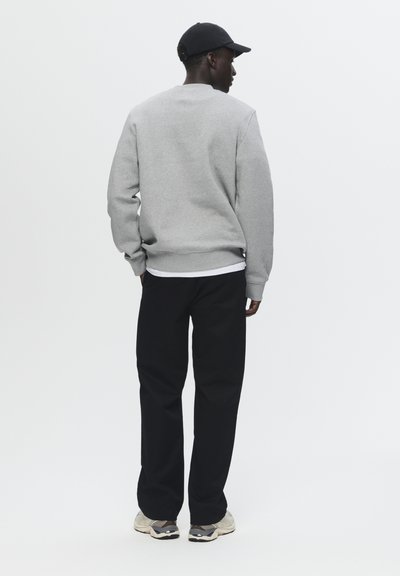 Grå sweatshirt med rund halsudskæring, ribbede manchetter, parret med sorte bukser og beige sneakers. Modellen står med ryggen til kameraet.