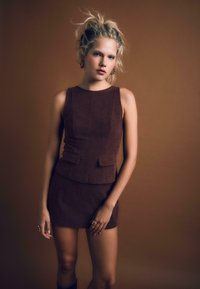 Top senza maniche in corduroy marrone con design aderente e tasche frontali, abbinato a una mini gonna coordinata, esposto su uno sfondo neutro.