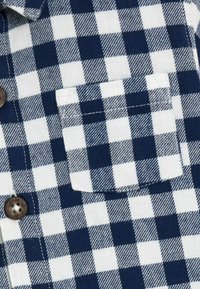 Blau-weißer karierter Stoff mit einer Tasche, braunen Knöpfen und einer strukturierten Webart mit abwechselnden Quadraten.