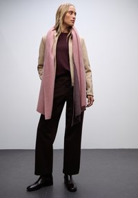 Cappotto beige, maglione bordeaux, pantaloni larghi marroni e una sciarpa a righe rosa. Texture liscia con stivali marroni lucidi. Design semplice e moderno.