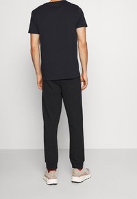 Zwarte katoenen T-shirt en bijpassende zwarte joggers, met elastische boorden. De joggers hebben zijzakken en zijn gecombineerd met lichtbeige sneakers.