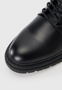 Bota de cuero negro con un acabado suave, punta redonda, suela de goma resistente y cordones con ojales de metal.