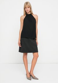 Czarny top na halter z zebranym dekoltem, w połączeniu z szaro-skalą sukienką A-line. Modelka nosi jasno-szare buty na szpilkach z wydłużonym noskiem. Minimalistyczny design, gładki materiał.