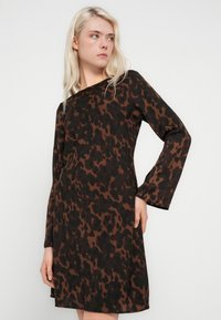 Rochie cu imprimeu leopard maro și negru, cu mâneci lungi, croială lejeră și tăietură dreaptă. Material neted, design până la nivelul genunchilor, detalii minimale.