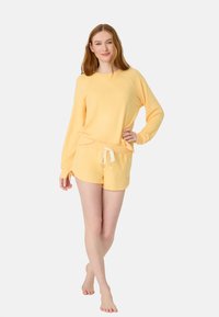 Set di abbigliamento comodo giallo composto da una maglietta a maniche lunghe e pantaloni corti coordinati. Il tessuto è morbido, con una vestibilità rilassata e una vita con cordino.